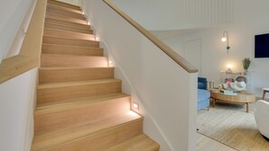 A staircase with wooden steps and a handrail, leading to a room with a blue sofa, a round wooden coffee table, and a wall-mounted TV. - Stroll to Shore, Modern Santa Rosa Beach Duplex! (Santa Rosa Beach)