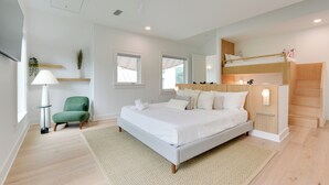 A modern bedroom with a large bed, a green chair, a bedside table, and a bunk bed. - Stroll to Shore, Modern Santa Rosa Beach Duplex! (Santa Rosa Beach)
