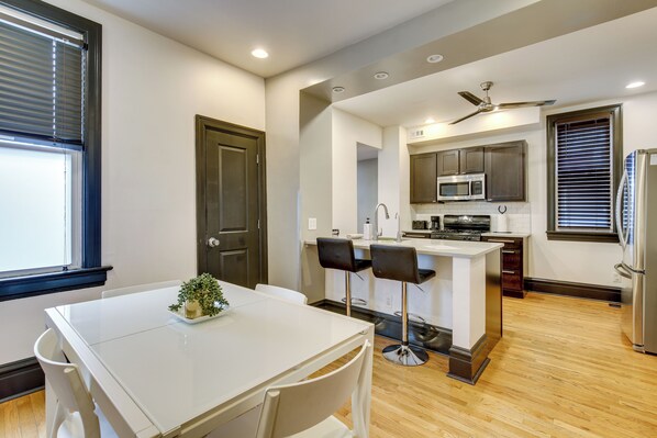 A modern kitchen with a central island, bar stools, and a dining table with chairs. - Walk to Tower Grove Park: St Louis Getaway (St. Louis)