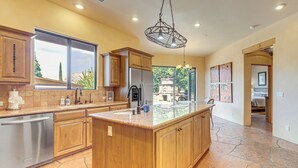 A spacious kitchen with a large island, wooden cabinets, and a stone tile floor. - 1/2 Mi to Airport Mesa! Hot Tub Haven w/ Mtn Views (Sedona)