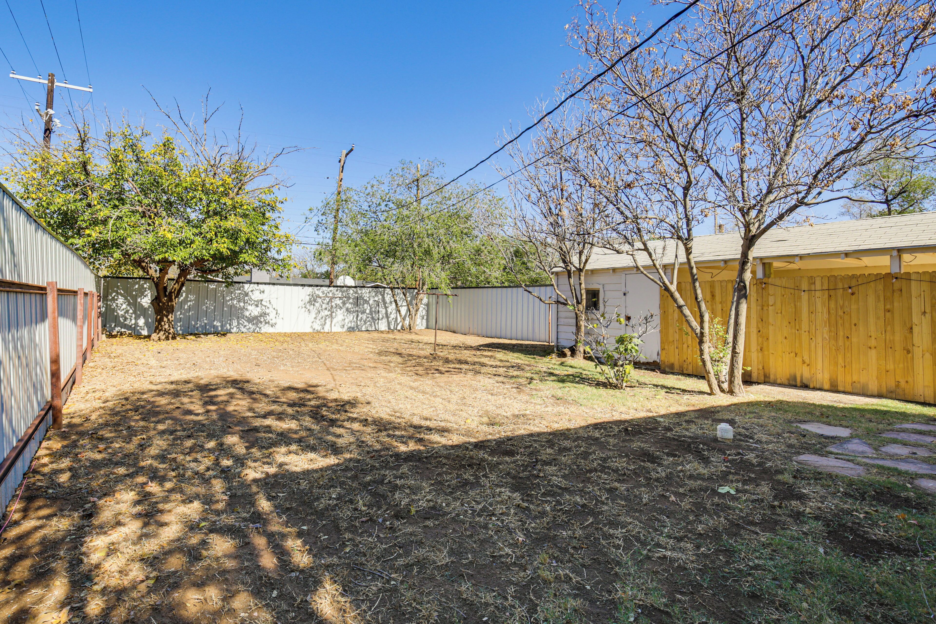 A backyard with a fenced area, a wooden shed, and a tree.