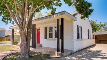 A single-story house with a red door, white exterior, and a tree in front.