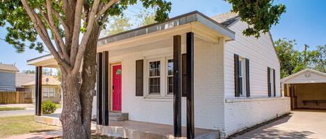 A single-story house with a red door, white exterior, and a tree in front.