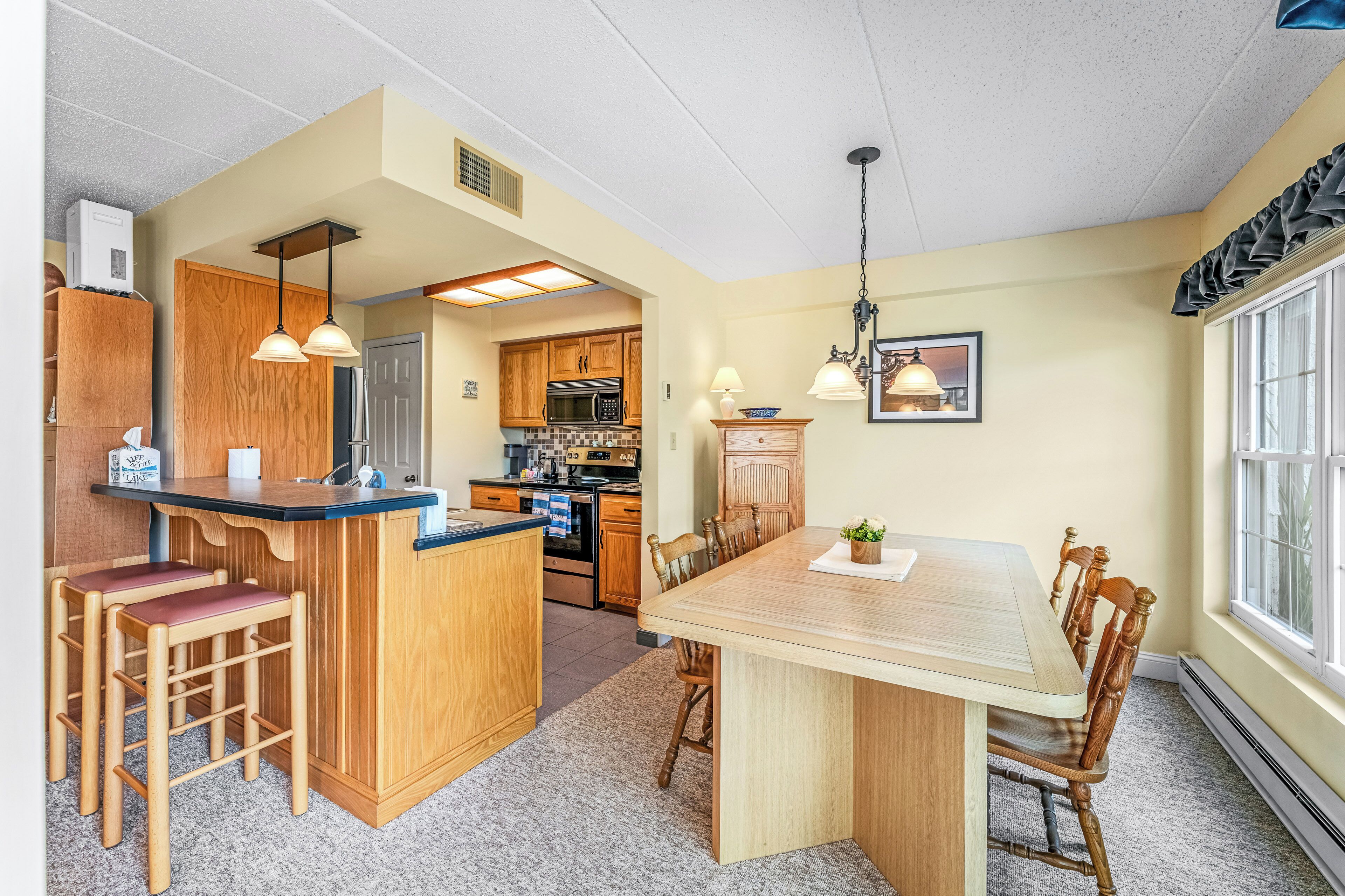 A kitchen with wooden cabinets, a central island with stools, and pendant lighting.