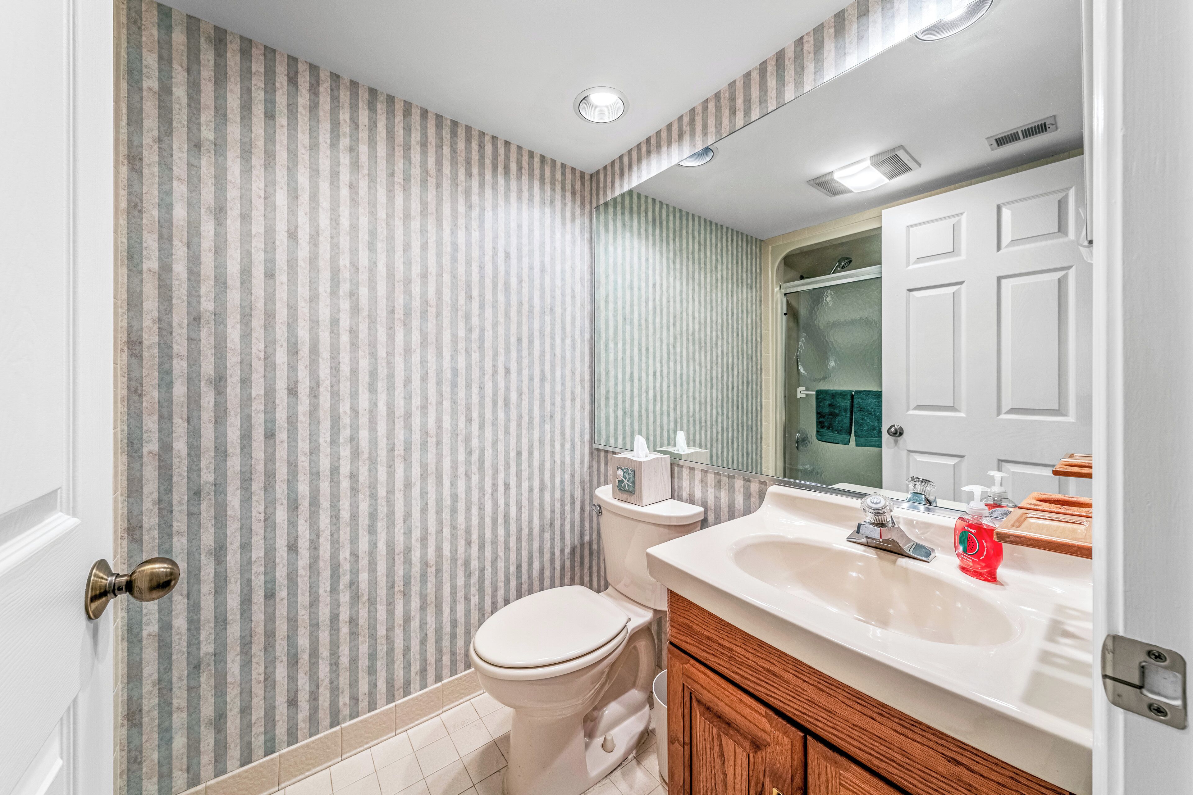 A bathroom with striped wallpaper, a white toilet, a sink with a mirror, and wooden cabinets.