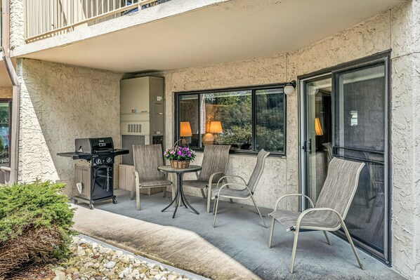 An outdoor patio with a grill, chairs, and a table with a flower arrangement.