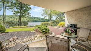 Eine Terrasse mit Korbmöbeln, einem Grill und Blick auf einen See und Wald.