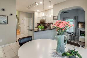 Una cucina moderna con mobili bianchi, un forno a microonde e un lavandino. C'è un tavolo da pranzo con sedie e un vaso di fiori.