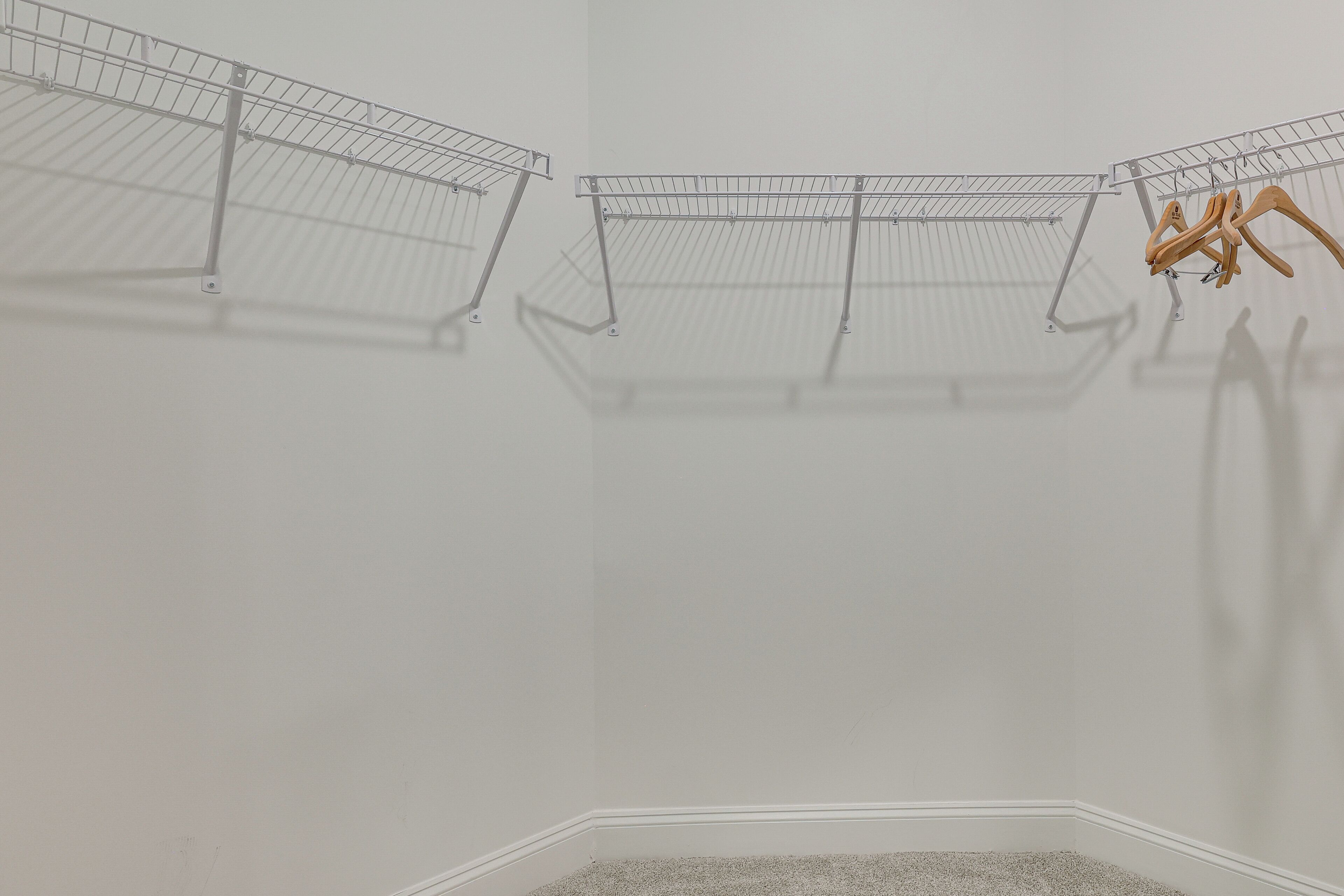 A corner of a room with three wire shelving units, one with wooden hangers, and a small carpeted area.