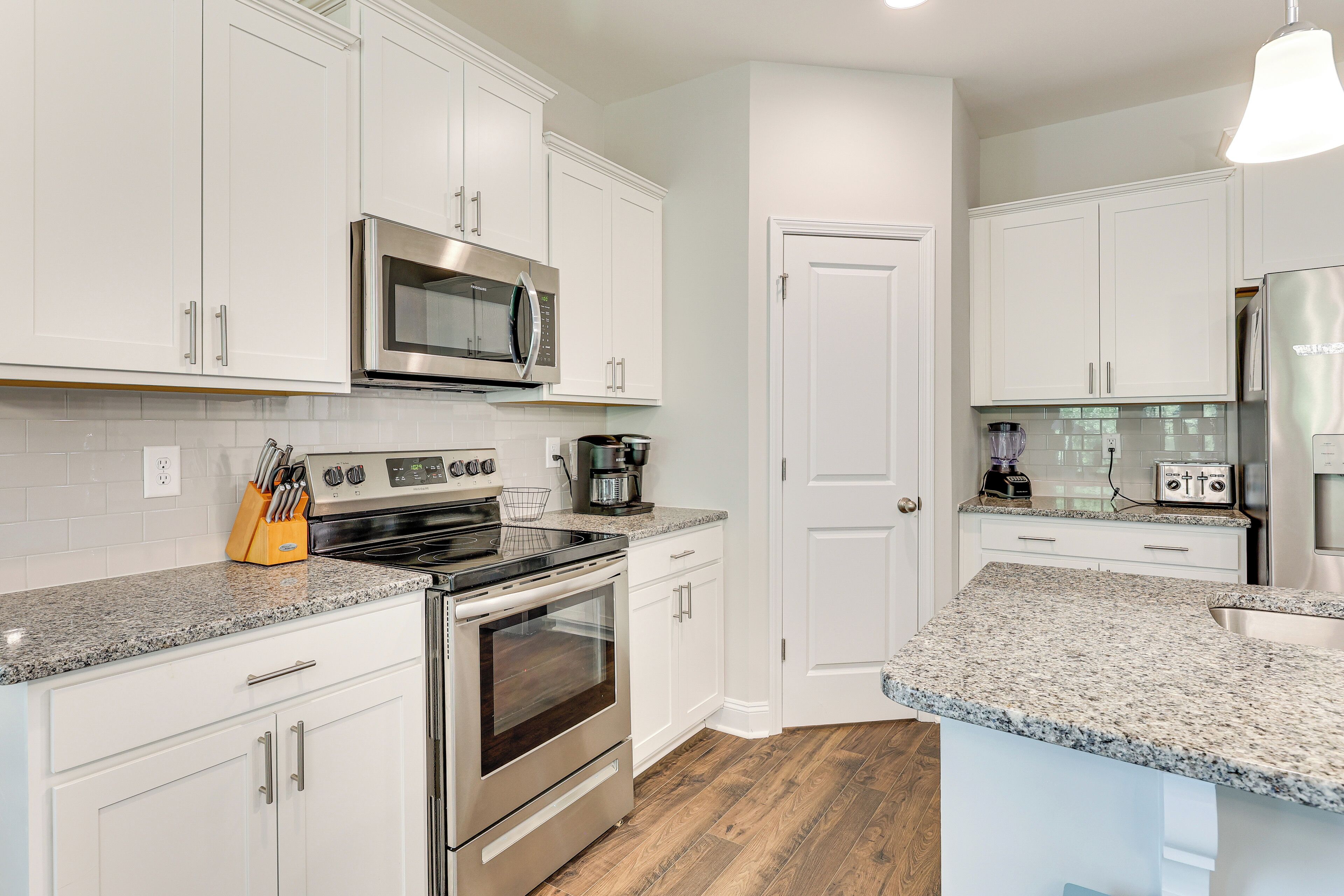 A modern kitchen with white cabinetry, stainless steel appliances, granite countertops, and a wooden floor.