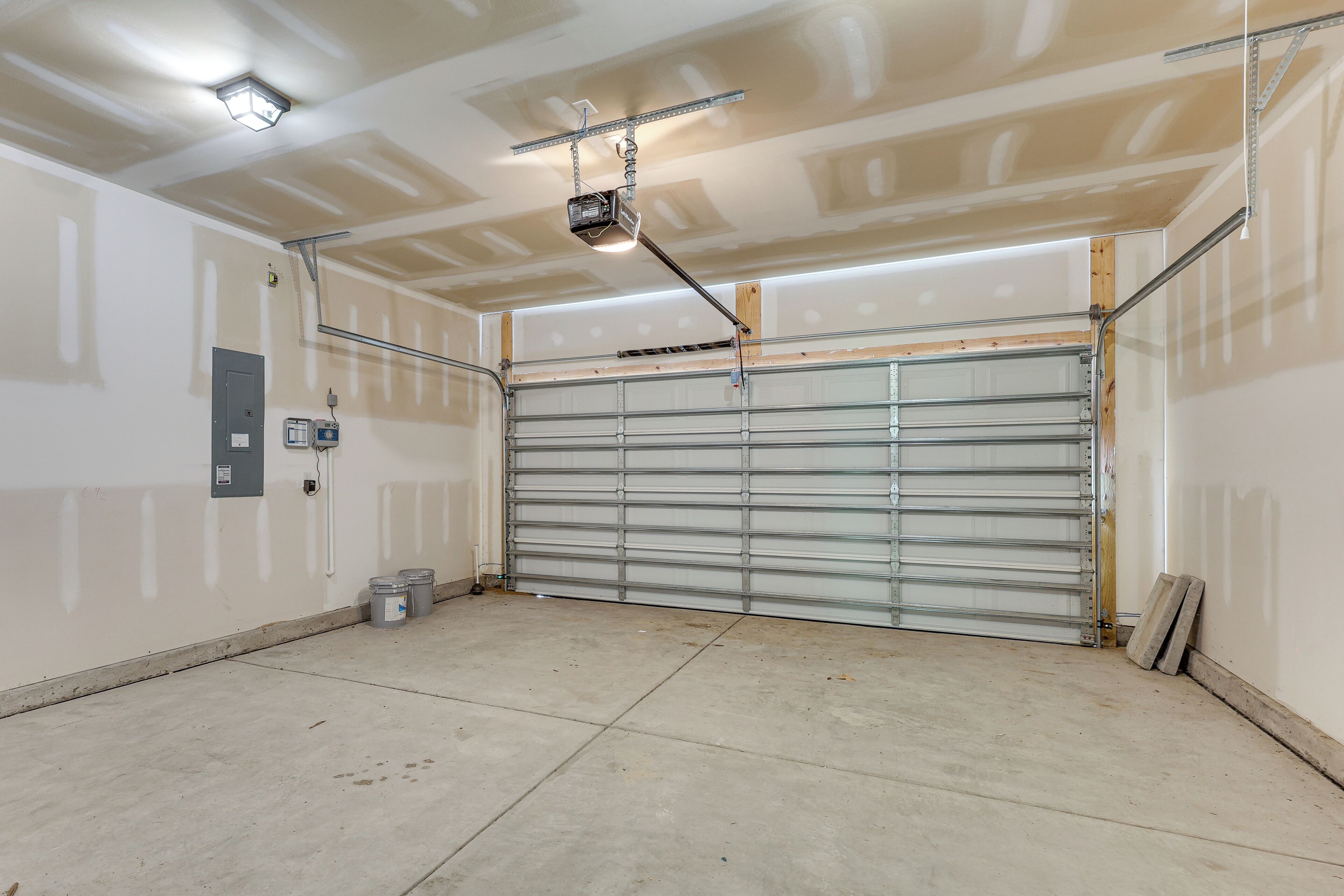 Uma garagem com porta metálica fechada, luminária no teto e uma tomada na parede.