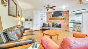 Una sala de estar con sofás de cuero, chimenea, televisor y una cocina al fondo.