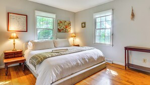 Un dormitorio con una cama grande, dos lámparas de noche, una mesita de madera, una ventana con vistas a la vegetación y un ventilador de techo.