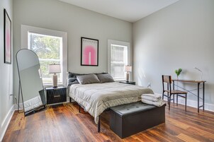 Un dormitorio con cama, mesitas de noche, un espejo, una banca y un escritorio con una silla.