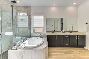 Une salle de bain moderne dotée d’une douche à parois de verre, d’une baignoire sur pieds, d’un meuble-lavabo avec deux vasques et de meubles de rangement aux couleurs sombres.