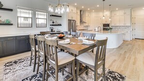 Une cuisine moderne avec des meubles blancs, un îlot central et un coin repas comprenant une table et des chaises en bois.