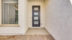Une maison avec une porte d’entrée sombre, une fenêtre ornée d’un rideau et un petit chemin de briques menant à la porte.