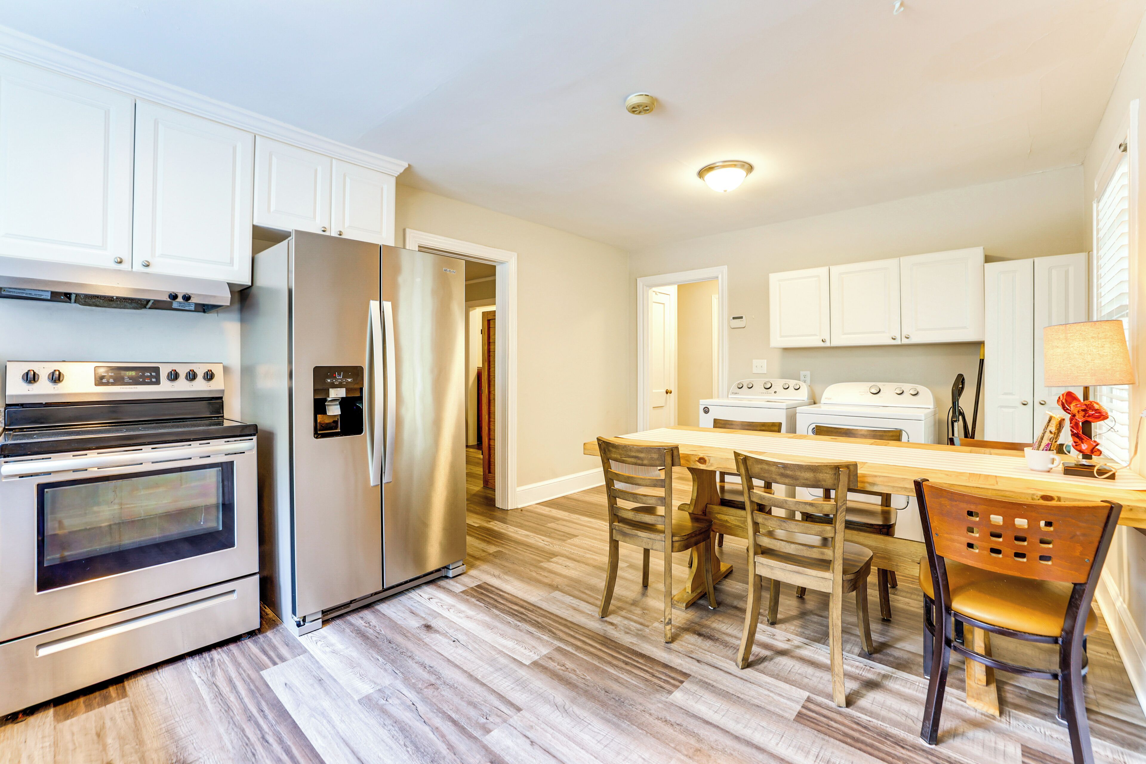 A kitchen with white cabinets, stainless steel appliances, a wooden dining table, and chairs.