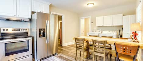 A kitchen with white cabinets, stainless steel appliances, a wooden dining table, and chairs.