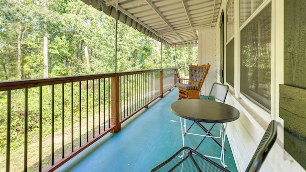 Une véranda couverte avec un plancher bleu, une balustrade en bois et une table entourée de chaises.