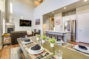 A modern kitchen with a stainless steel refrigerator, a dining area with a long table set for four, and a living room with a leather sofa and a flat-screen TV. - Room to Work + Relax! SLC Townhome w/ Office, Yard (Salt Lake City)