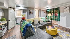 Un salon moderne avec un canapé d’angle, un pouf jaune et un coin repas agrémenté d’un buffet blanc.