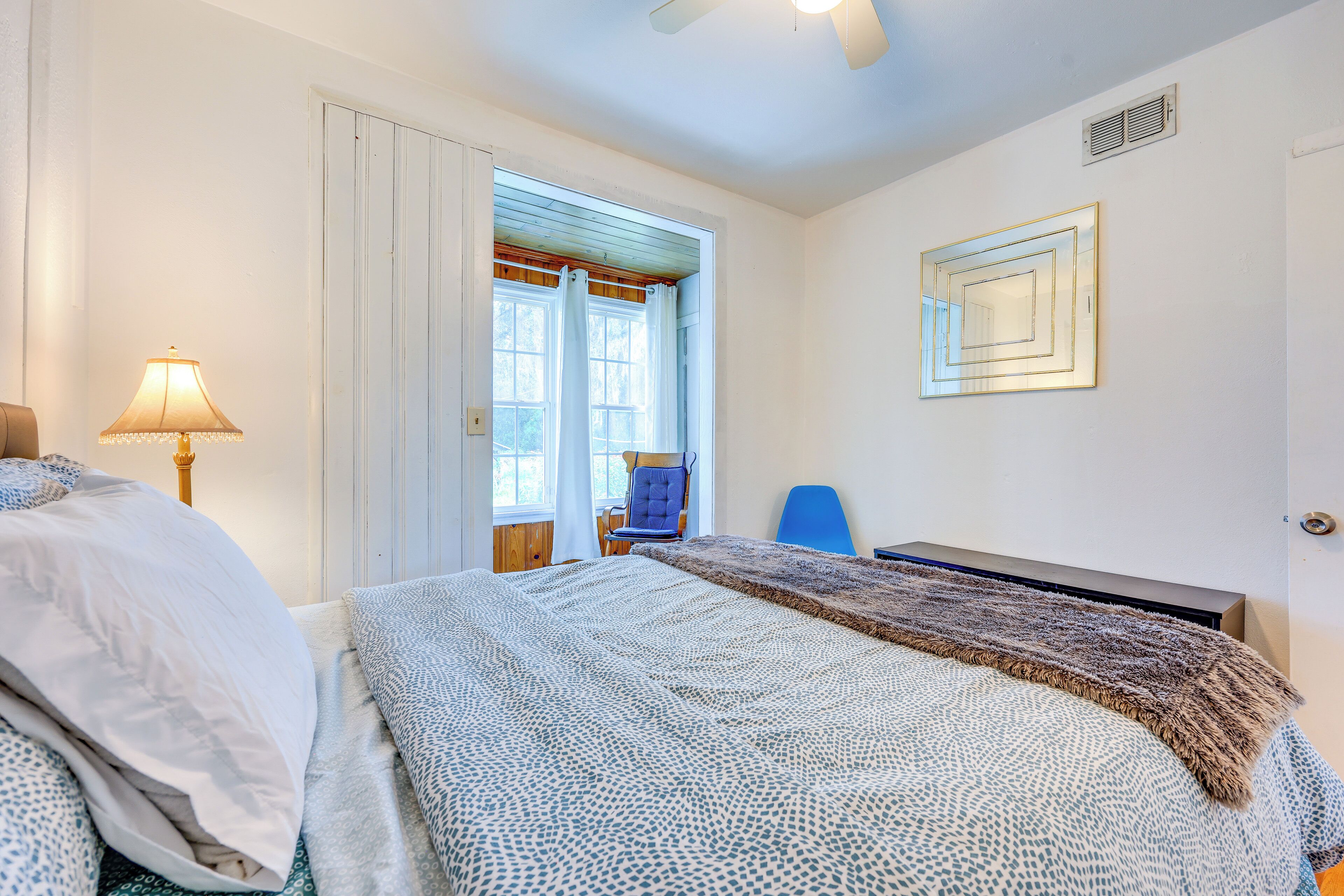 Ein Schlafzimmer mit Bett, Schreibtisch, Stuhl, Lampe und einem Fenster mit Vorhängen.