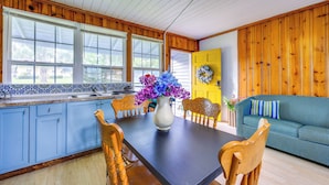 Et køkken med træskabe, et spisebord med stole, en vase med blomster og en blåstribet sofa.