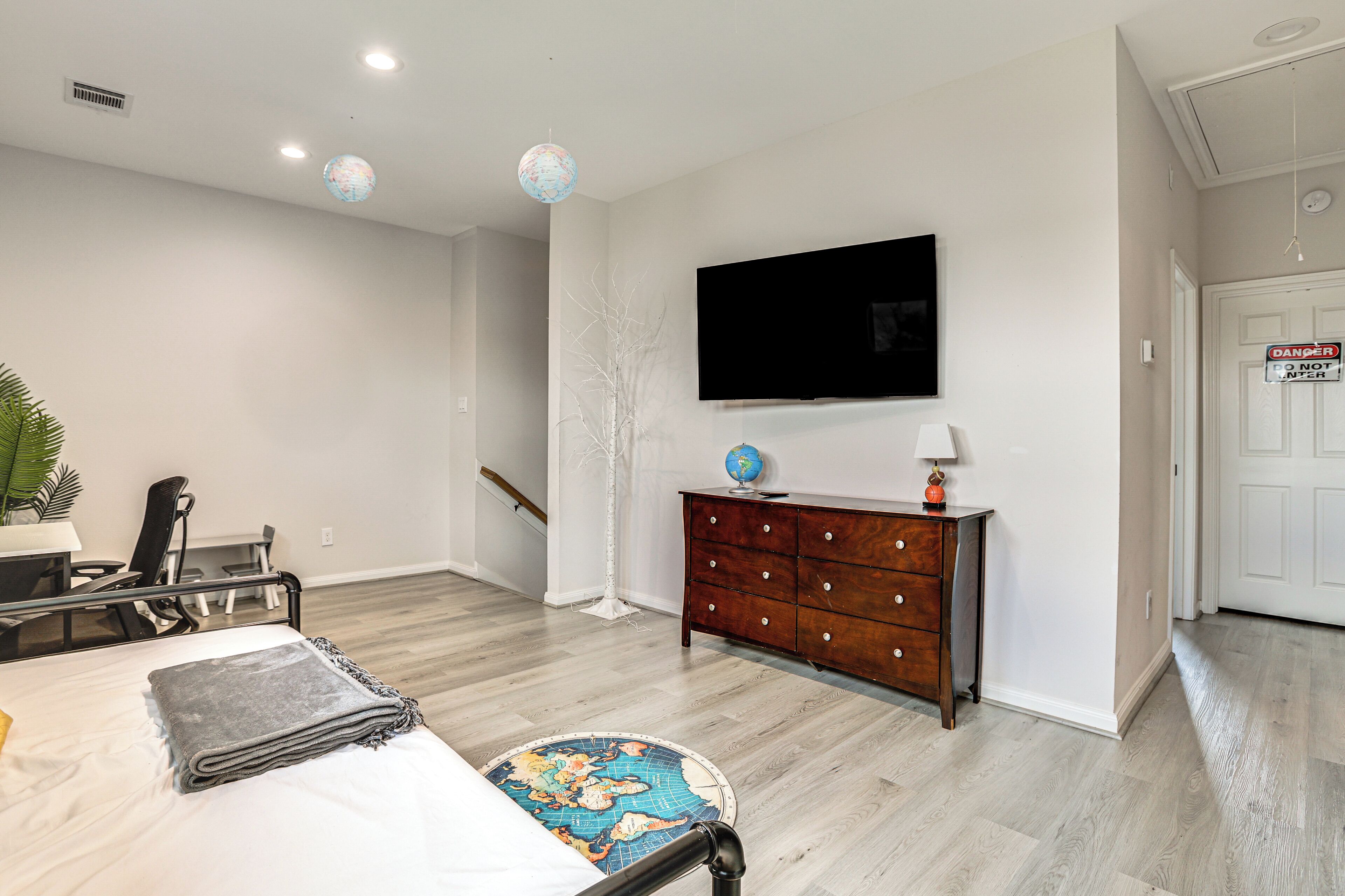 A modern hotel room with a bed, a desk, a dresser, a globe, and a television.