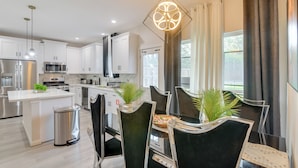 A modern kitchen with white cabinets, stainless steel appliances, and a dining area with black chairs and a central island. - 10 Mi to Downtown Houston: Family Home w/ Yard (Houston)
