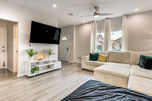 A modern living room with a flat-screen TV, a white entertainment unit, a beige sofa, and a ceiling fan. - 10 Mi to Downtown Houston: Family Home w/ Yard (Houston)