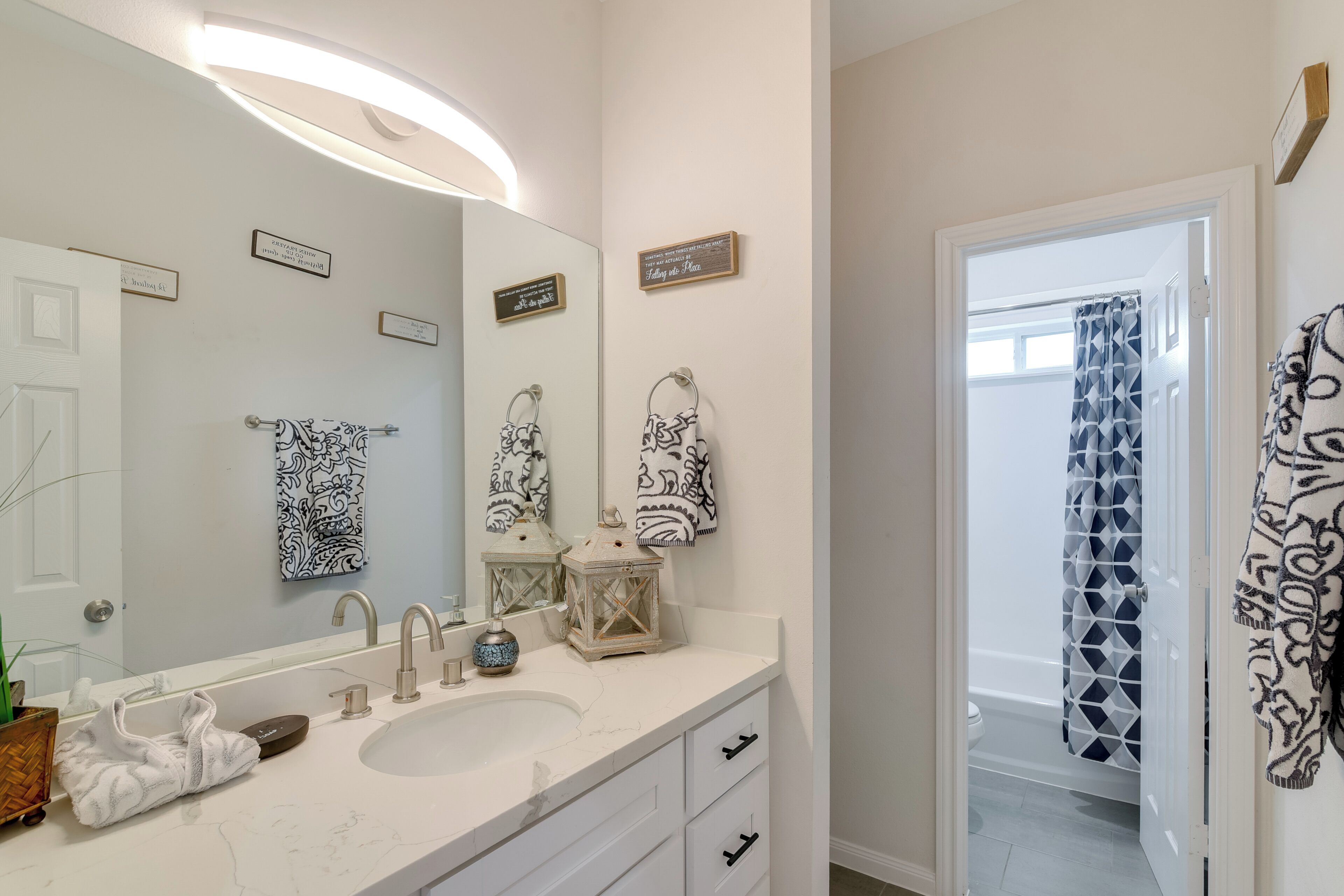 A bathroom with a large mirror, two sinks, a vanity with drawers, and a shower curtain with a geometric pattern.