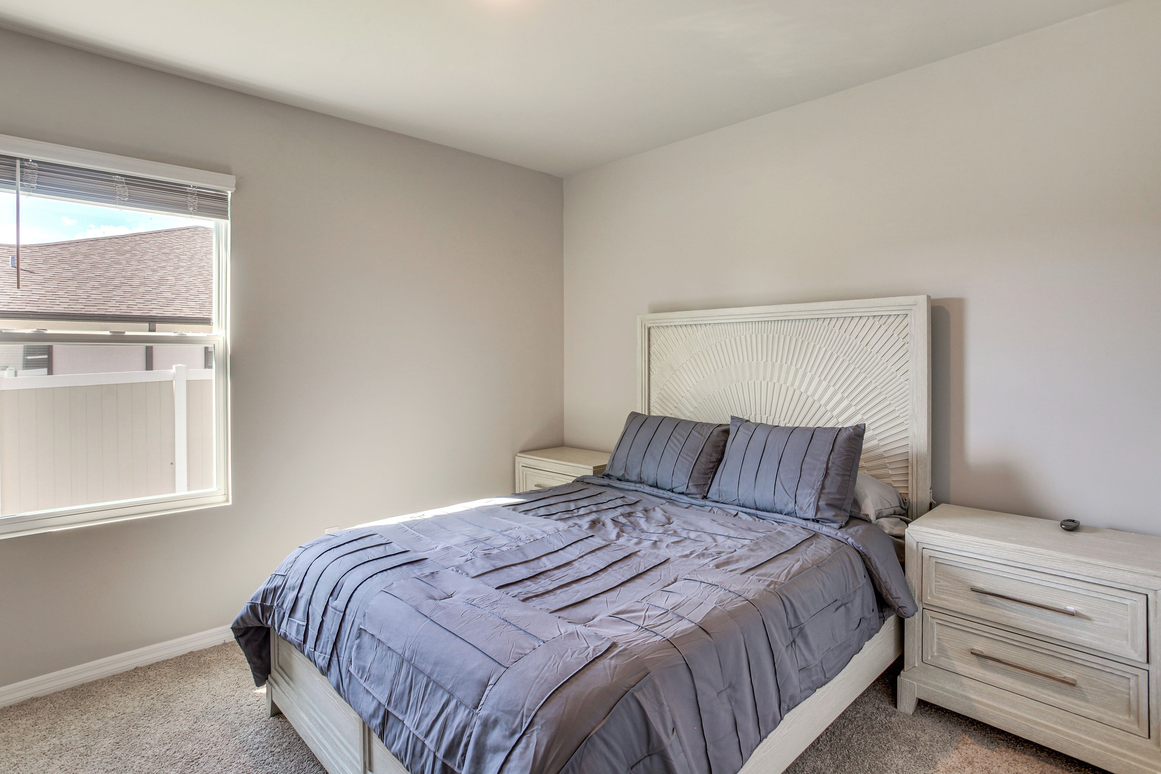 A bedroom with a bed, nightstands, a window, and a headboard.