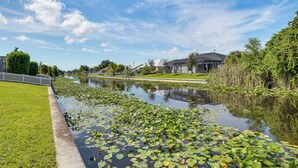 Un plan d’eau paisible, parsemé de nénuphars, entouré d’une pelouse bien entretenue et bordé d’une rangée de maisons.