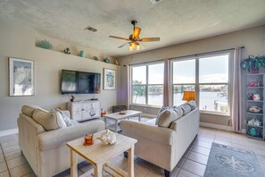 A living room with a sofa, a coffee table, a TV, and a large window with a view of a body of water. - Boat Dock & Patio: Cape Coral Home 6 Mi to Beach! (Cape Coral)