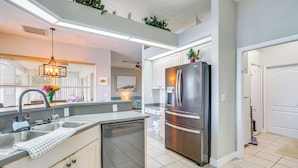 A modern kitchen with a stainless steel refrigerator, a dishwasher, and a large window with blinds.
