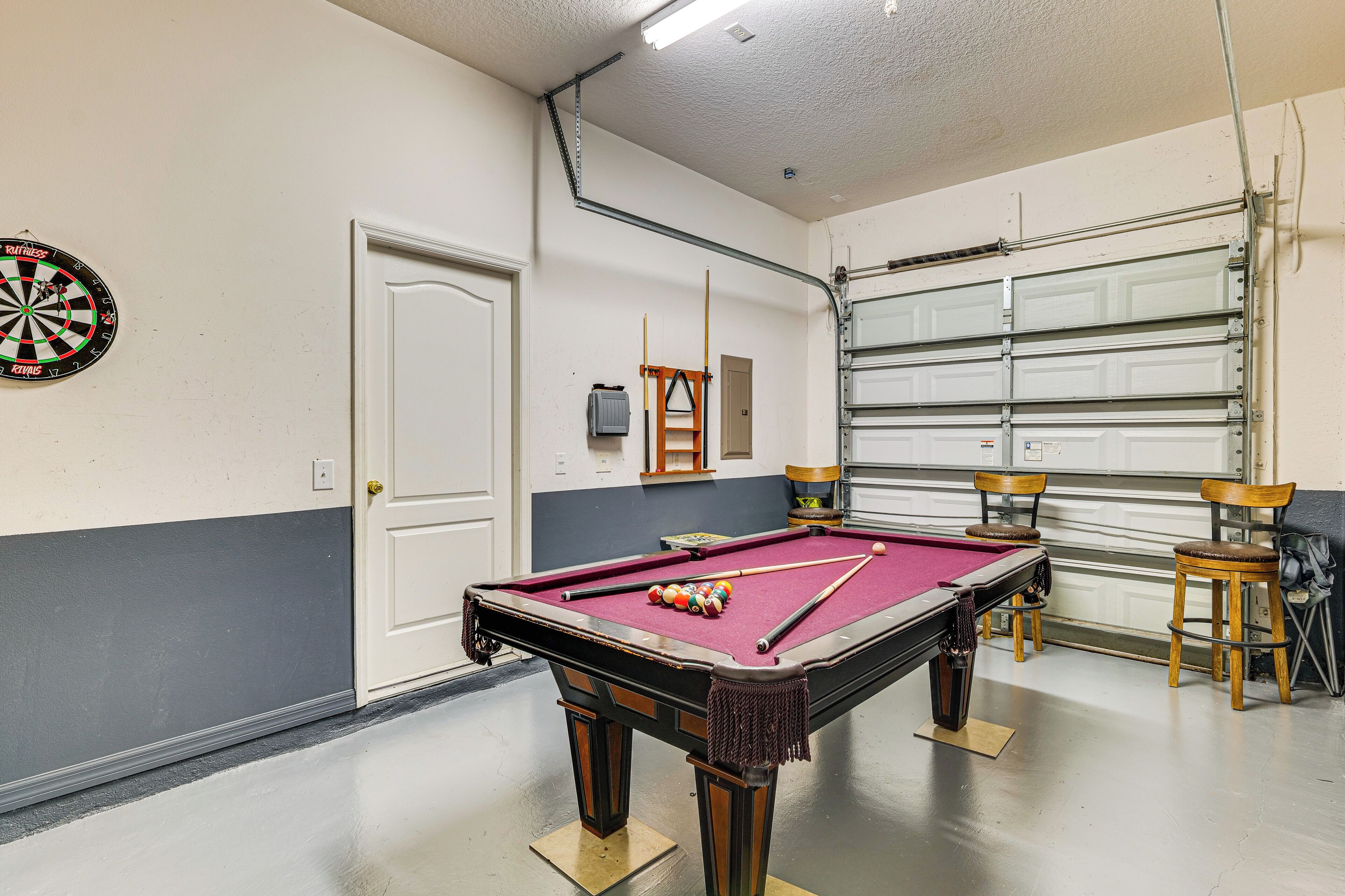 Une table de billard avec des billes, un jeu de fléchettes et deux chaises en bois.