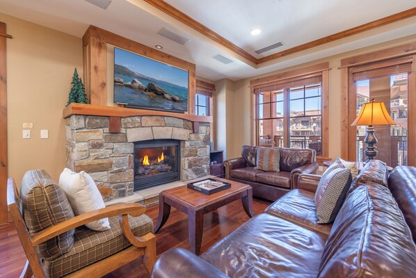 A cozy living room with a stone fireplace, leather furniture, and large windows overlooking a scenic view.
