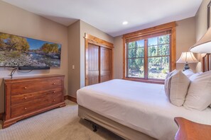 A bedroom with a large bed, wooden dresser, and a window with a view of trees.