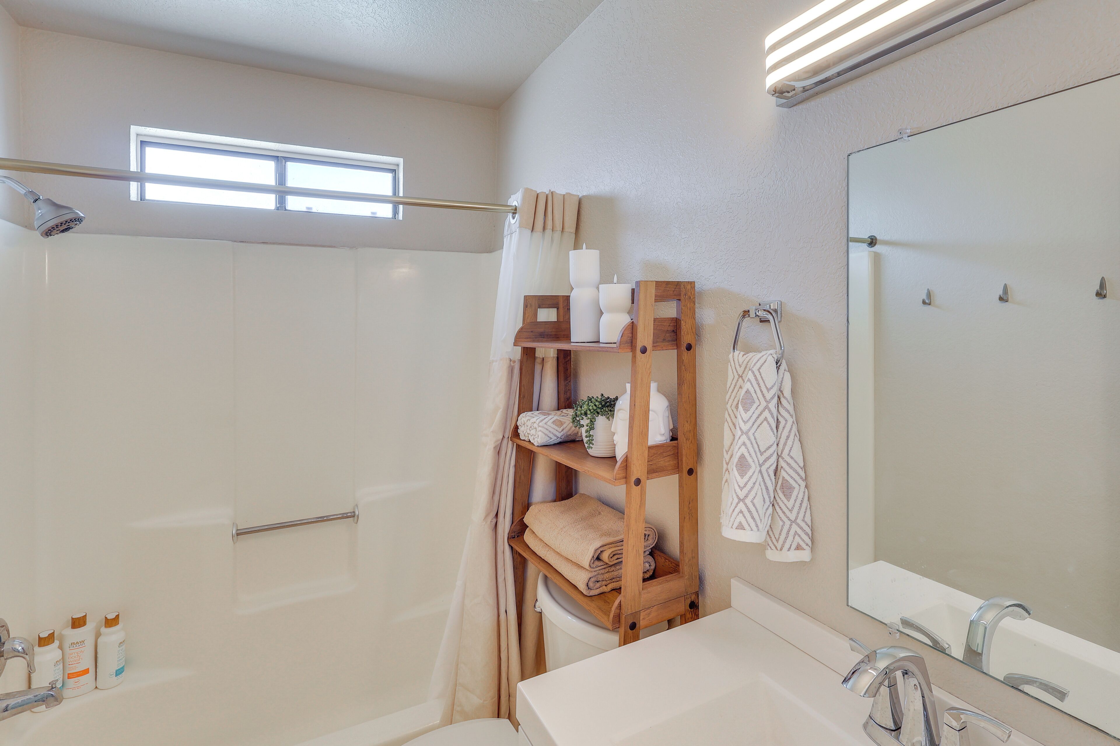 Ein Badezimmer mit Dusche, einem Holzboden mit Handtüchern und Toilettenartikeln, einem großen Spiegel und einem Fenster für natürliches Licht.