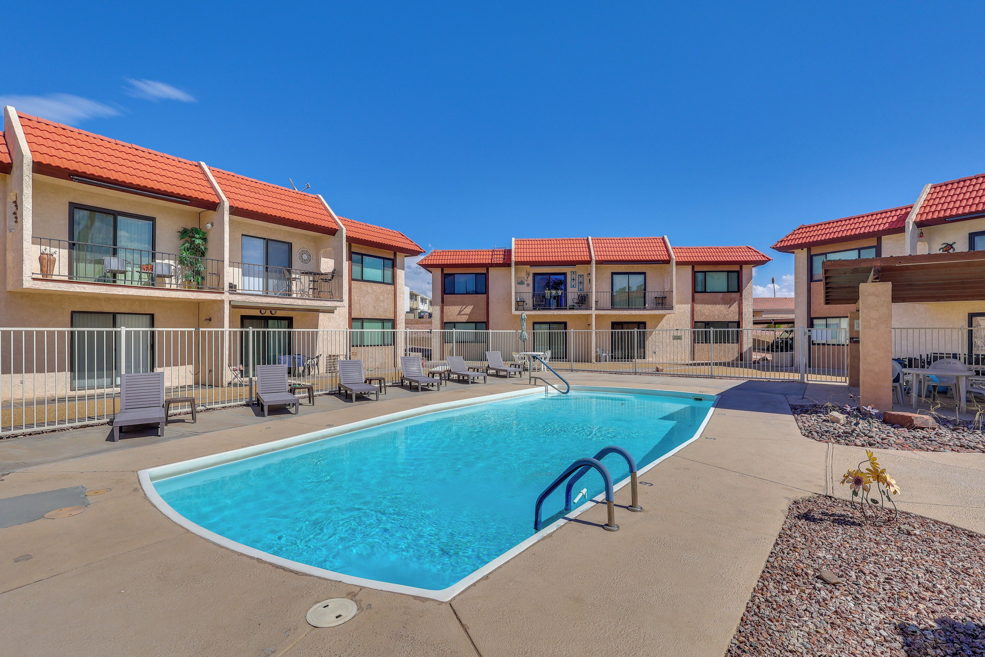 A swimming pool with lounge chairs and a building with red-tiled roofs.