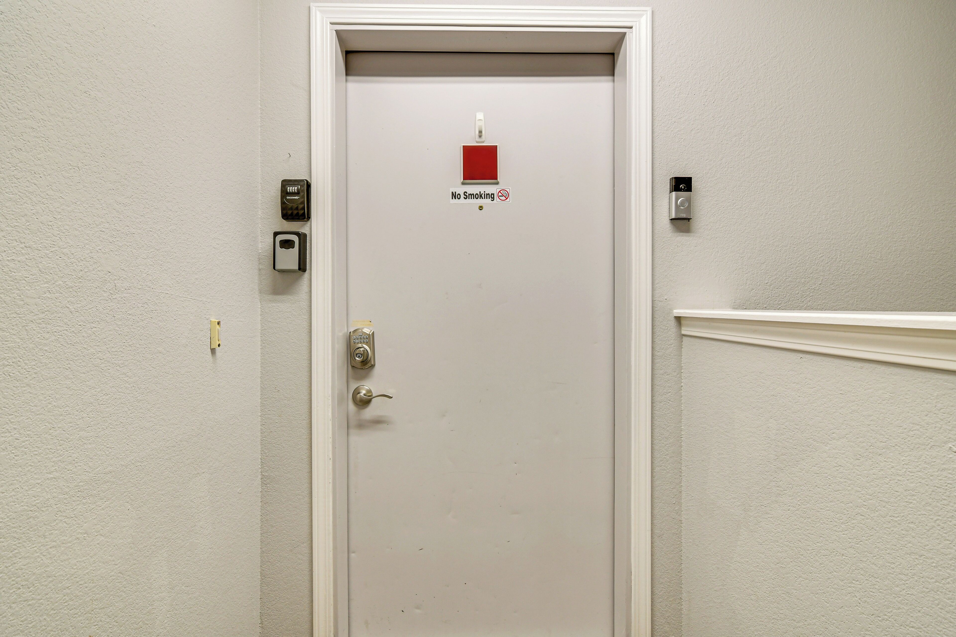 Eine weiße Tür mit einem Rauchverbotsschild, Klingel und Sicherheitsschloss.