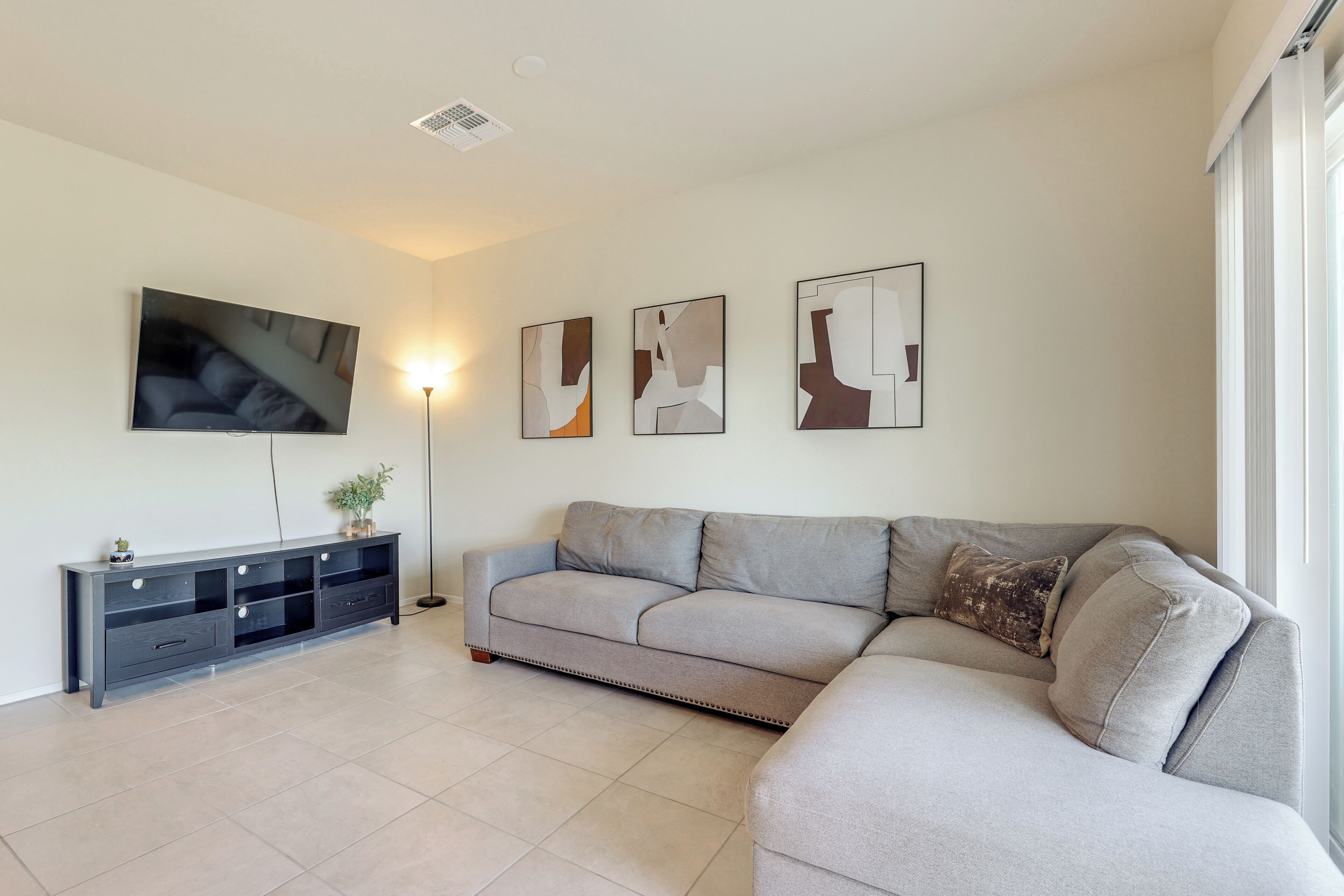 A modern living room with a grey sofa, a flat-screen TV, a dark wooden console, and abstract wall art.