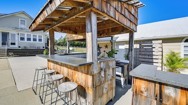 Eine hölzerne Bar im Freien mit Barhocker und Theke, umzäunt und mit einem Haus im Hintergrund.
