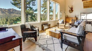 Un salon spacieux doté de grandes fenêtres, de meubles en bois et offrant une vue sur une colline boisée.