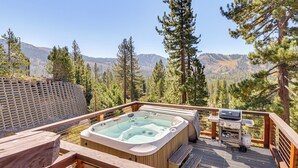 Un bain à remous sur une terrasse en bois, avec vue sur les montagnes et les arbres.