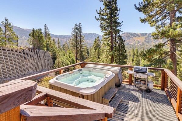 Un bain à remous sur une terrasse en bois, avec vue sur les montagnes et les arbres.