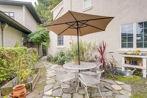 A patio with a round table and chairs, a large umbrella, and a garden with various plants. - Walkable Miracle Mile Retreat w/ Peaceful Patio (Stockton)