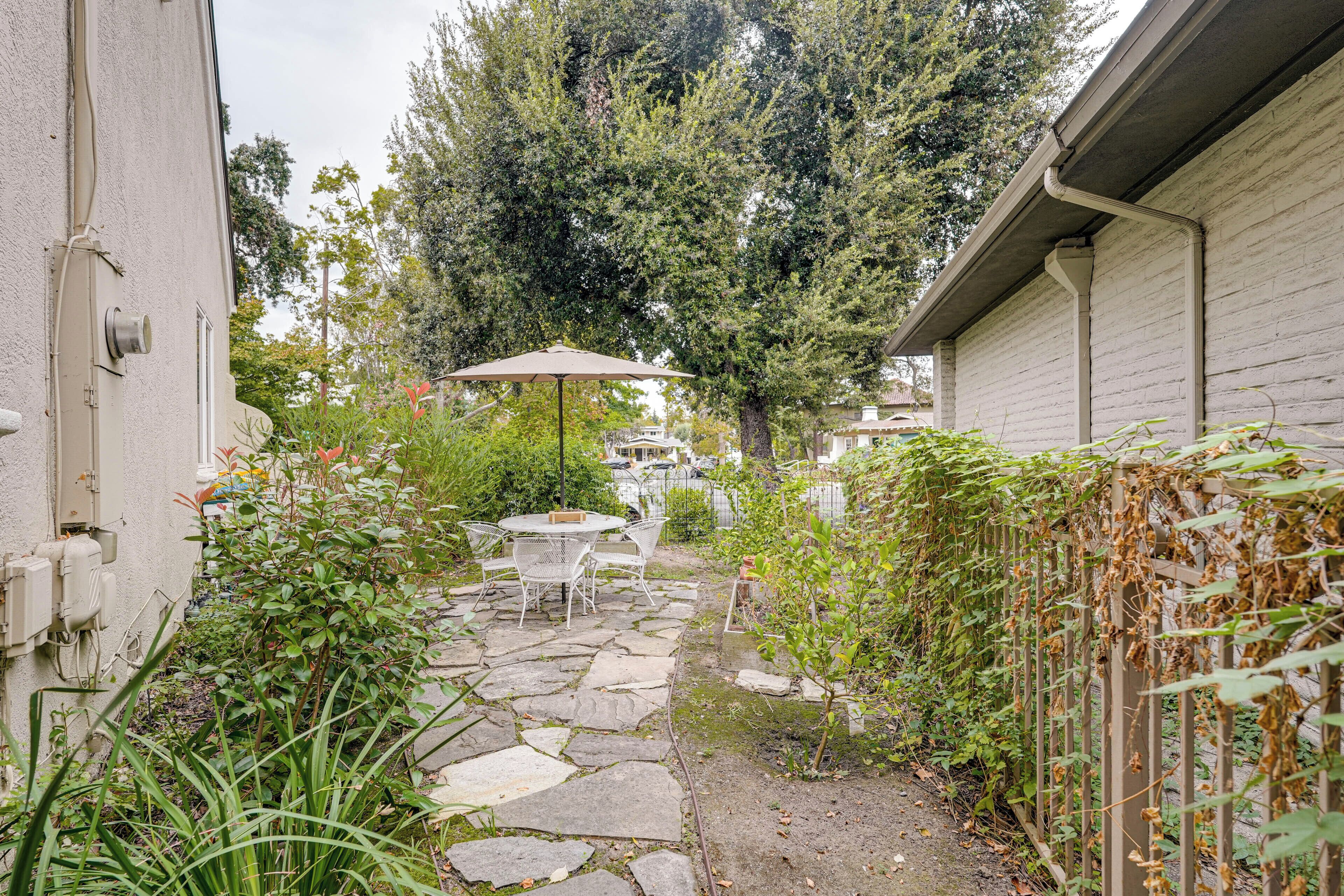 A stone-paved patio with outdoor furniture, surrounded by greenery and trees.