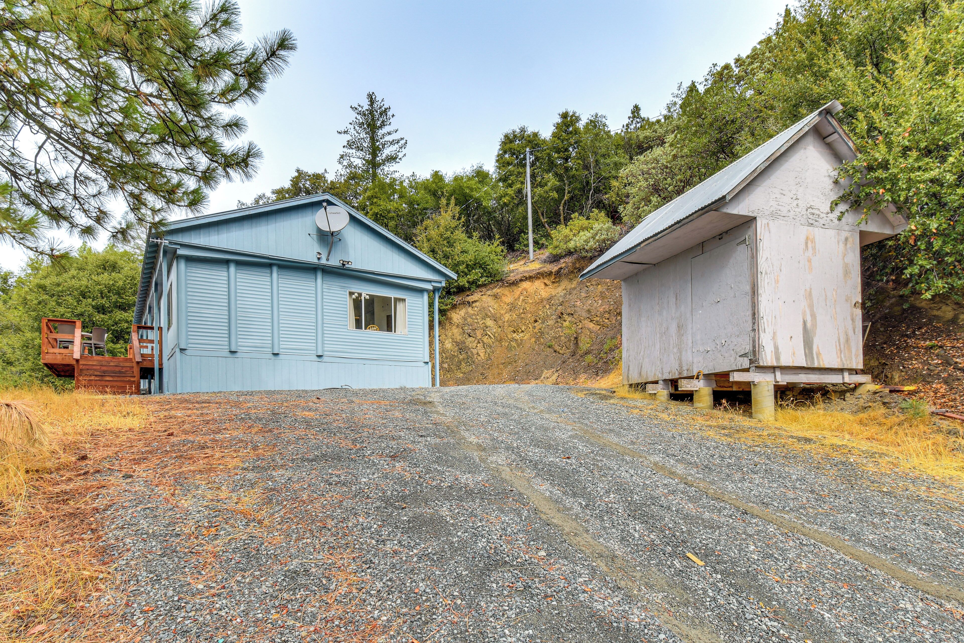 A gravel driveway leading to a blue building with a satellite dish and a white building with a sloped roof.